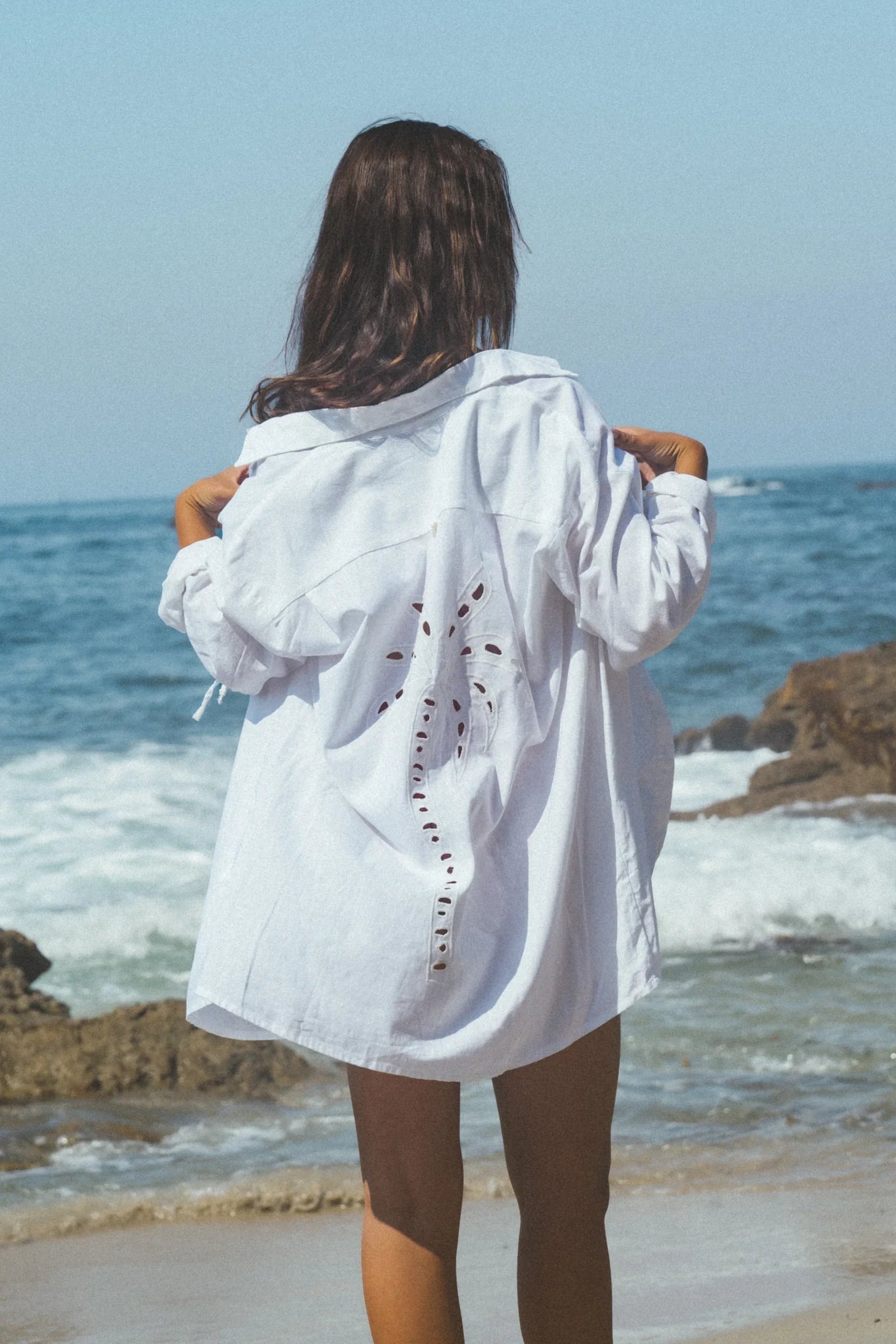 White collared shirt with buttons down the front, ties on the sleeves, and an eyelet palm tree design on the back.