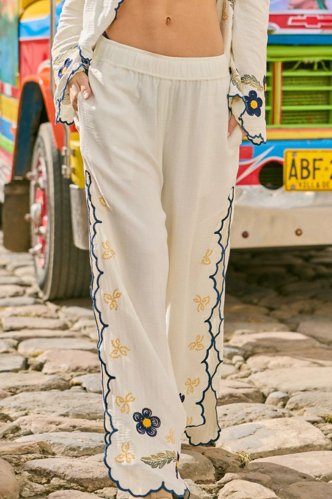 White wide leg pants with elastic waistband and blue and yellow embroidered floral print