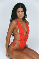 Red one piece with a deep plunging neckline, open back and sides, and skimpy coverage in the back