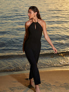 Sleeveless jumpsuit with a high neckline and keyhole cutout featuring gold hardware and a halter tie. Available in Black