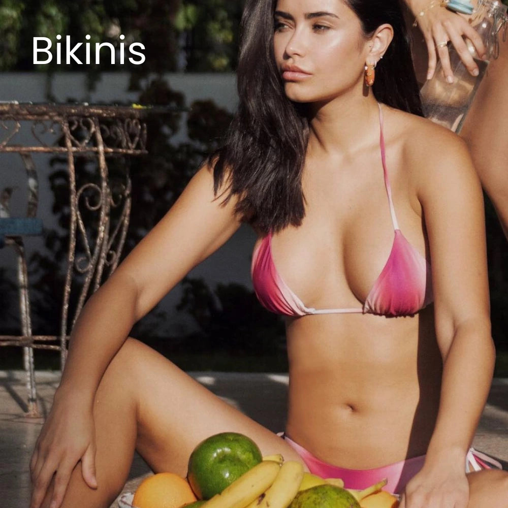 Close-up of a model wearing a Xandra Swimwear pink ombre bikini top, accessorized with hoop earrings, next to a selection of tropical fruits.
